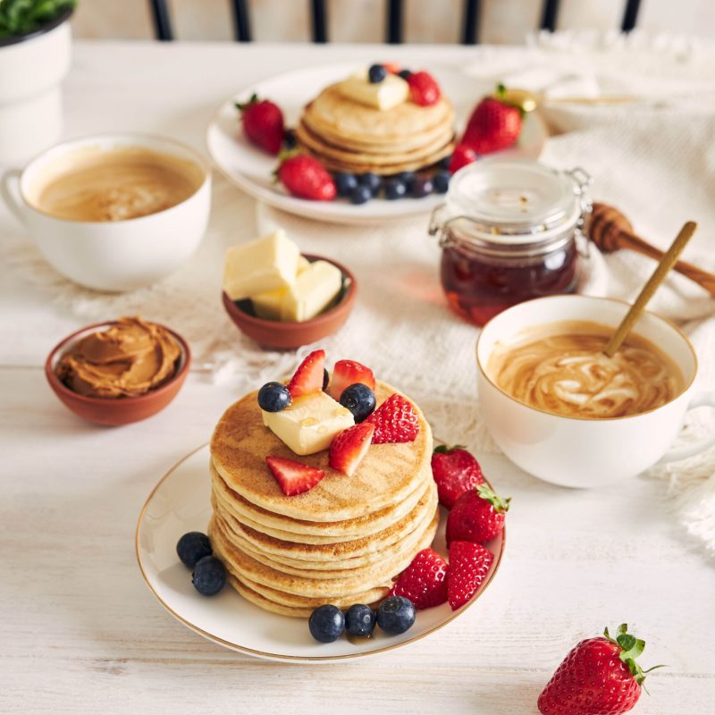 A vertical shot of Delicious vegan Tofu Pancakes with colorful Fruits, Syrup  and Coffee on a white wood Table